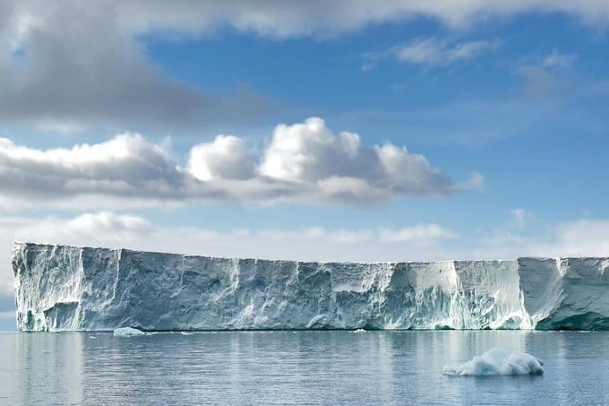 Desprendimiento masivo de hielo glaciar en primer plano, con un glaciar de fondo visiblemente reducido por el retroceso, mostrando la pérdida de hielo polar.